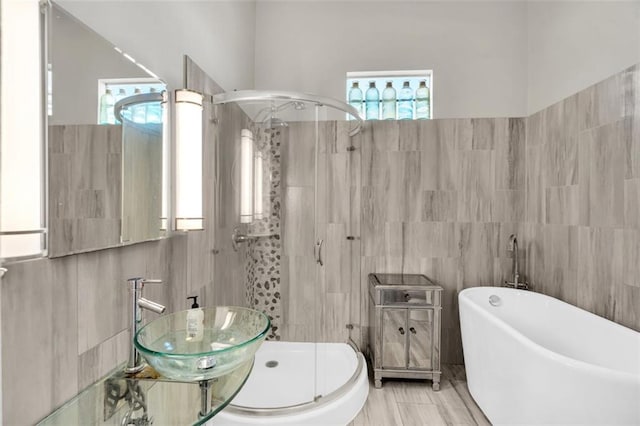 bathroom with a stall shower, a freestanding tub, a sink, and tile walls