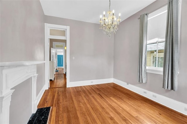 unfurnished dining area featuring an inviting chandelier, baseboards, and wood finished floors