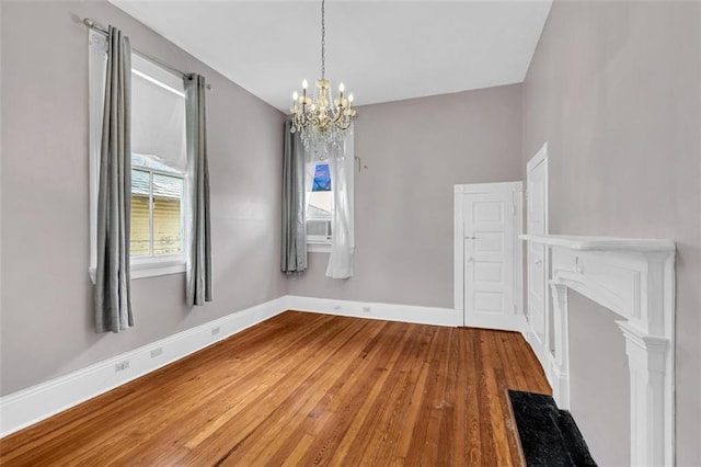 unfurnished dining area with an inviting chandelier, cooling unit, baseboards, and wood finished floors