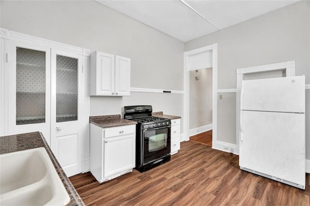 kitchen featuring dark wood finished floors, freestanding refrigerator, white cabinetry, black gas stove, and a sink