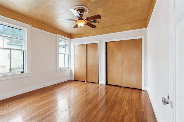 unfurnished bedroom with ceiling fan, light hardwood / wood-style floors, and multiple closets