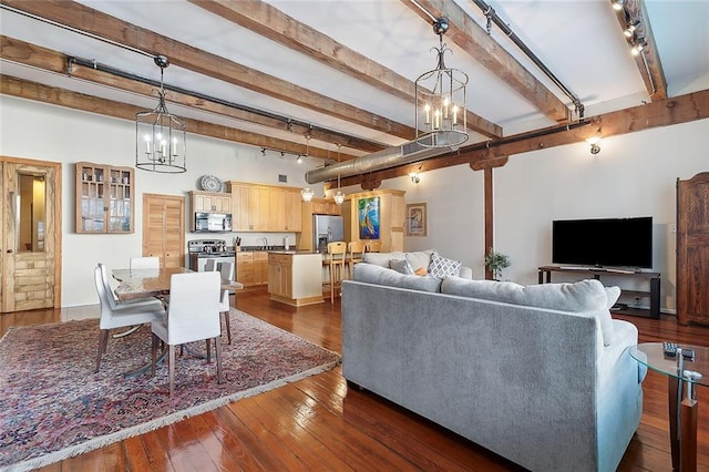 living room featuring dark hardwood / wood-style flooring, rail lighting, an inviting chandelier, and beamed ceiling