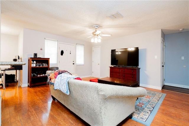 living room featuring ceiling fan, a textured ceiling, baseboards, and wood finished floors