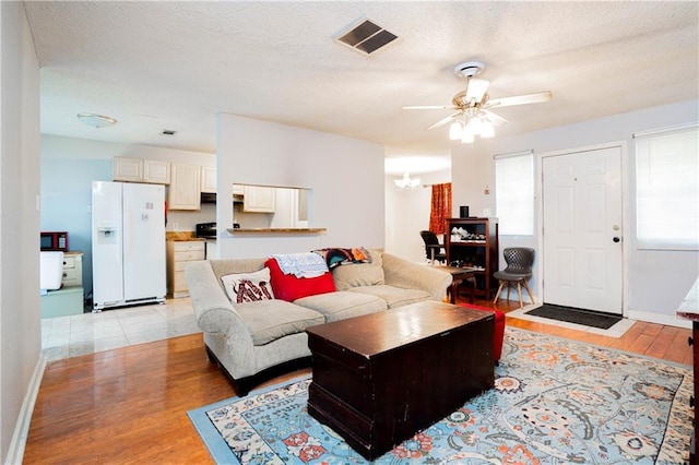 living area featuring light wood-style floors, visible vents, a textured ceiling, and ceiling fan with notable chandelier