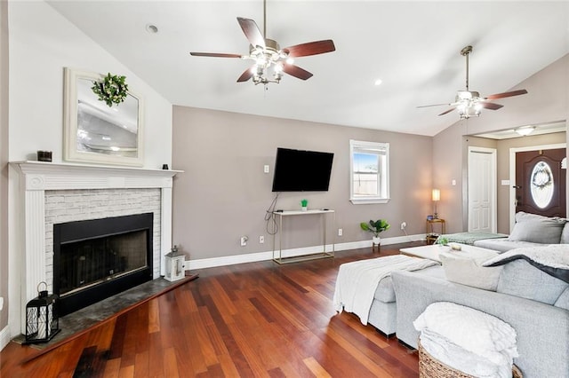 interior space with dark wood-type flooring, vaulted ceiling, a brick fireplace, and ceiling fan