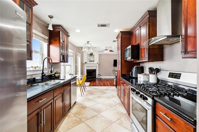 kitchen with light tile patterned floors, stainless steel appliances, sink, wall chimney exhaust hood, and ceiling fan