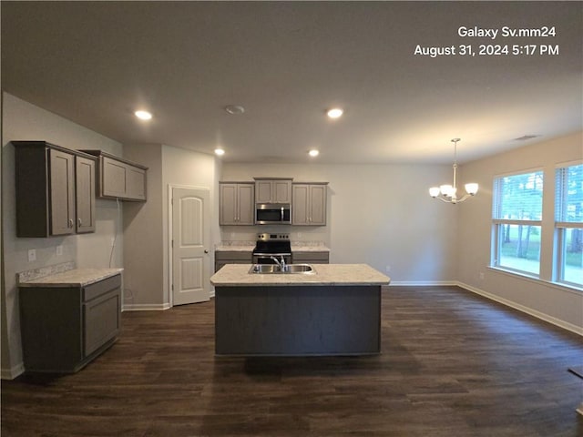 kitchen featuring an inviting chandelier, appliances with stainless steel finishes, light stone counters, dark wood-type flooring, and a center island with sink