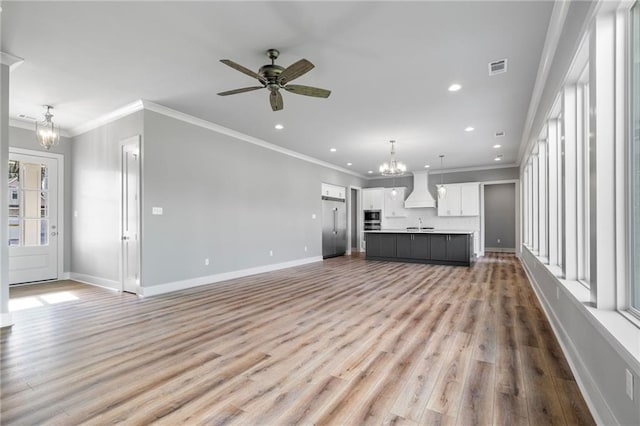 unfurnished living room featuring light wood-type flooring, ceiling fan with notable chandelier, and ornamental molding