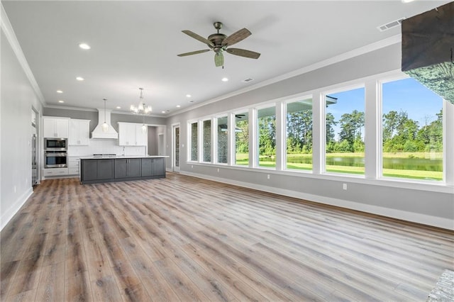 unfurnished living room with a water view, ceiling fan with notable chandelier, ornamental molding, and light hardwood / wood-style flooring