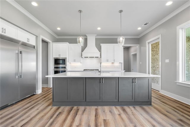 kitchen with built in appliances, custom range hood, and white cabinets