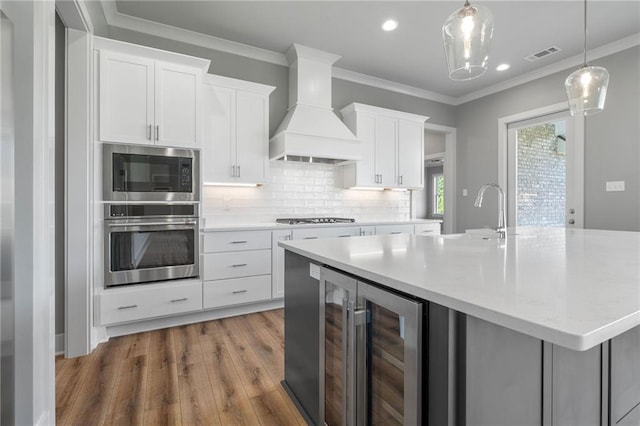 kitchen featuring light hardwood / wood-style flooring, custom range hood, beverage cooler, stainless steel appliances, and white cabinetry