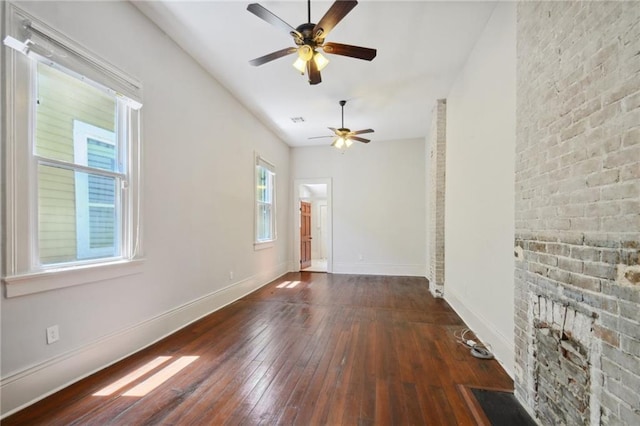 spare room featuring a fireplace, dark hardwood / wood-style flooring, a healthy amount of sunlight, and ceiling fan