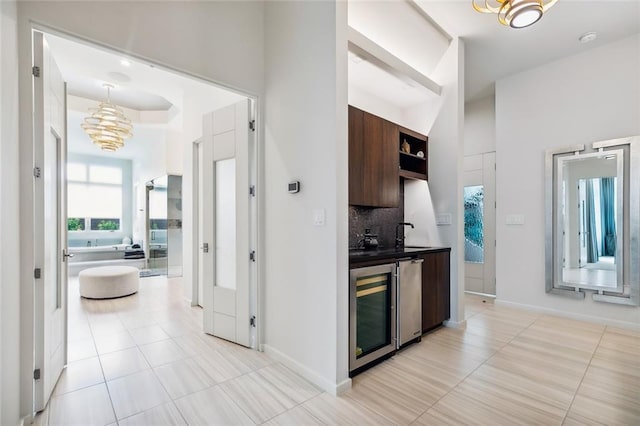 kitchen featuring wine cooler, a notable chandelier, light tile patterned floors, backsplash, and sink