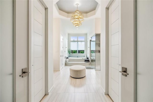 hallway featuring a raised ceiling, a notable chandelier, and light tile patterned floors