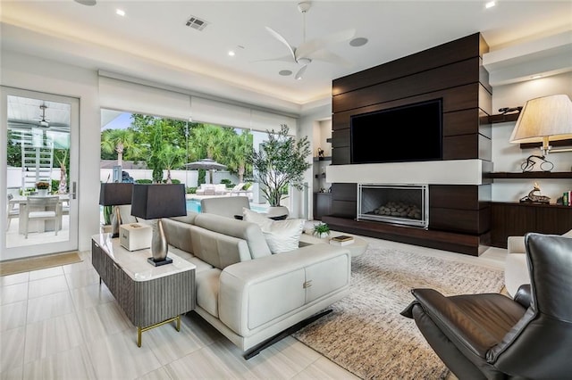 tiled living room with a tray ceiling, ceiling fan, and a fireplace