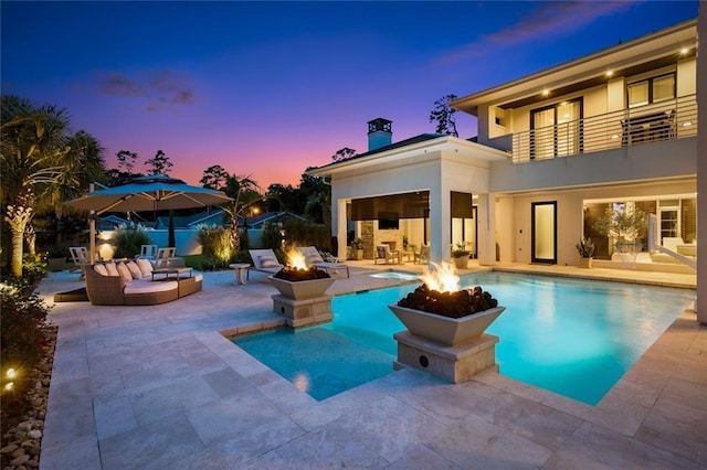 pool at dusk featuring an outdoor living space with a fire pit and a patio