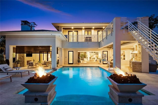 back house at dusk featuring a fire pit, a balcony, and a patio