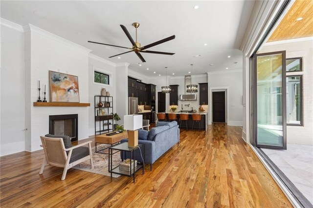 living room with a fireplace, crown molding, ceiling fan with notable chandelier, and light hardwood / wood-style flooring