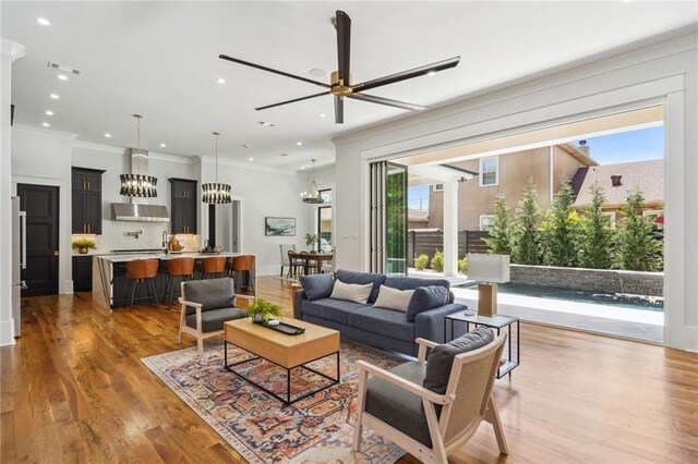 living room with ornamental molding, ceiling fan with notable chandelier, a wealth of natural light, and hardwood / wood-style floors