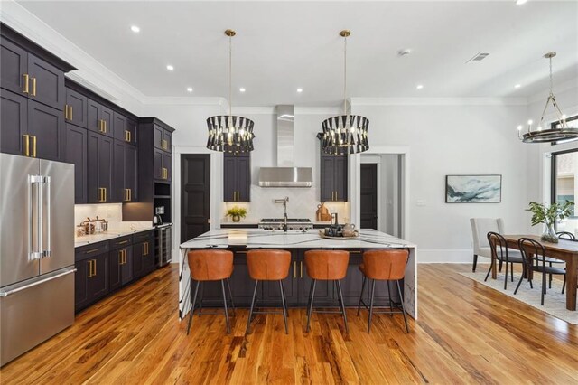 kitchen featuring wall chimney exhaust hood, high end refrigerator, a breakfast bar, hardwood / wood-style flooring, and a large island