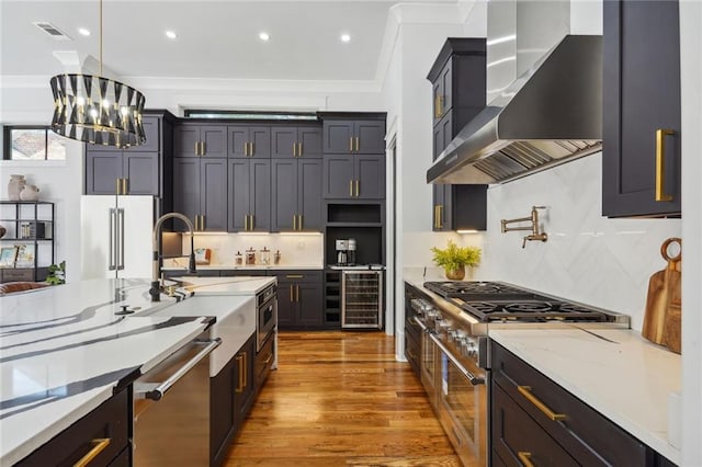 kitchen with decorative light fixtures, hardwood / wood-style floors, stainless steel appliances, ornamental molding, and wall chimney range hood