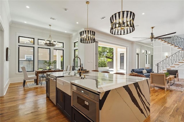 kitchen featuring light stone countertops, light hardwood / wood-style floors, a notable chandelier, a kitchen island with sink, and stainless steel microwave