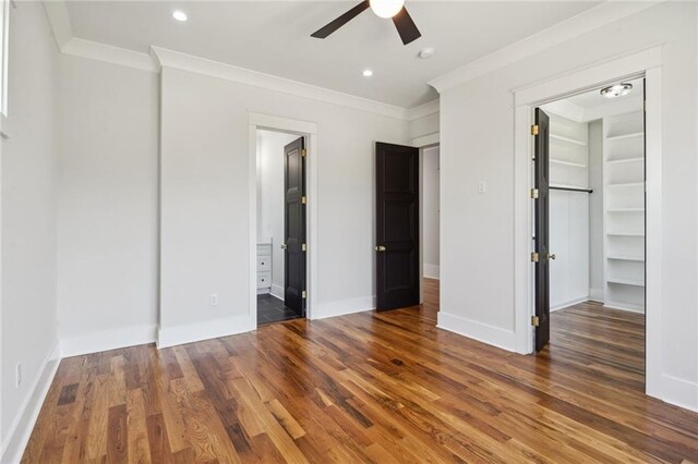 unfurnished bedroom with crown molding, ceiling fan, a spacious closet, and dark hardwood / wood-style flooring