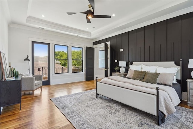 bedroom with light hardwood / wood-style flooring, a tray ceiling, access to outside, ornamental molding, and ceiling fan