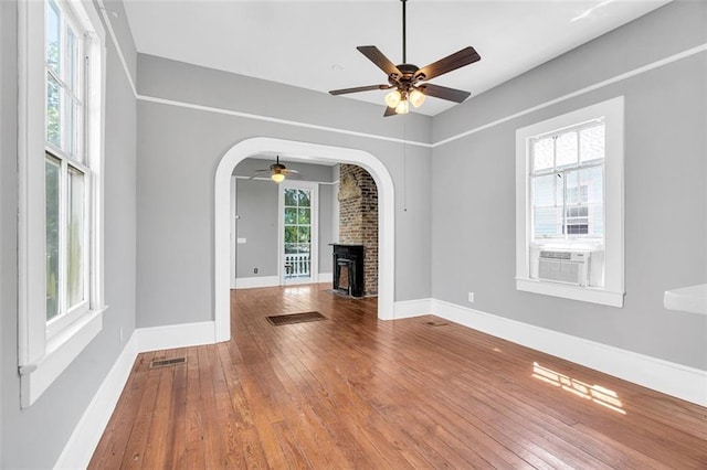 unfurnished living room with hardwood / wood-style flooring, plenty of natural light, a brick fireplace, and ceiling fan