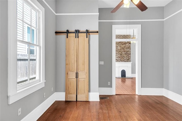 unfurnished bedroom featuring hardwood / wood-style floors, ceiling fan, and a barn door