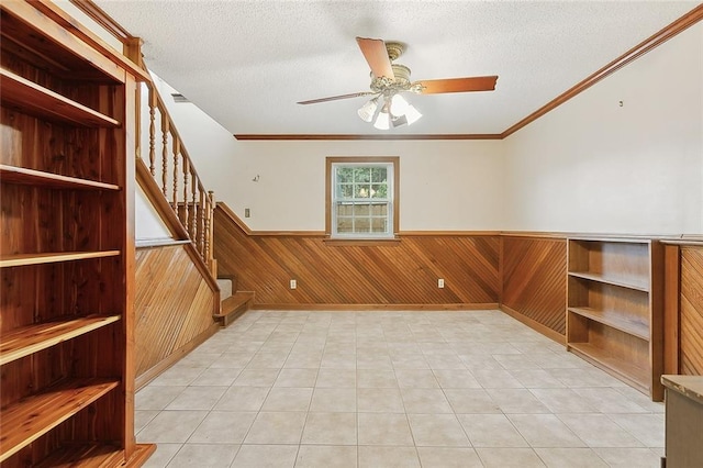 tiled empty room featuring a textured ceiling, crown molding, ceiling fan, and wooden walls