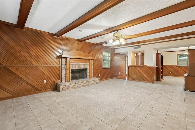 unfurnished living room with wooden walls, beam ceiling, a fireplace, and a ceiling fan