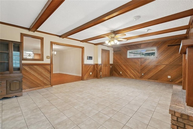 unfurnished living room with beam ceiling, a ceiling fan, a wood stove, wood walls, and a textured ceiling