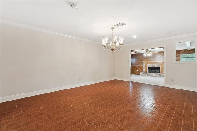 unfurnished living room featuring a fireplace, wooden walls, ceiling fan with notable chandelier, dark wood-type flooring, and ornamental molding