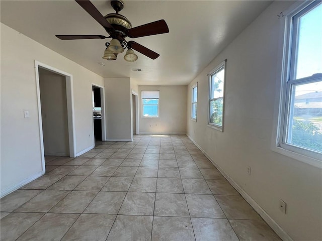 empty room with a healthy amount of sunlight, light tile patterned flooring, and ceiling fan