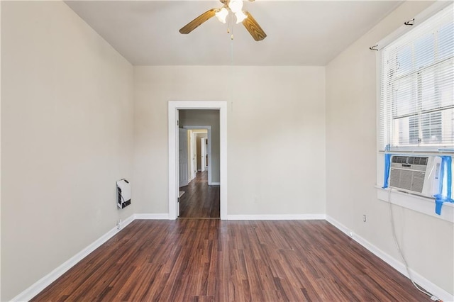 empty room featuring wood finished floors, baseboards, a ceiling fan, and heating unit