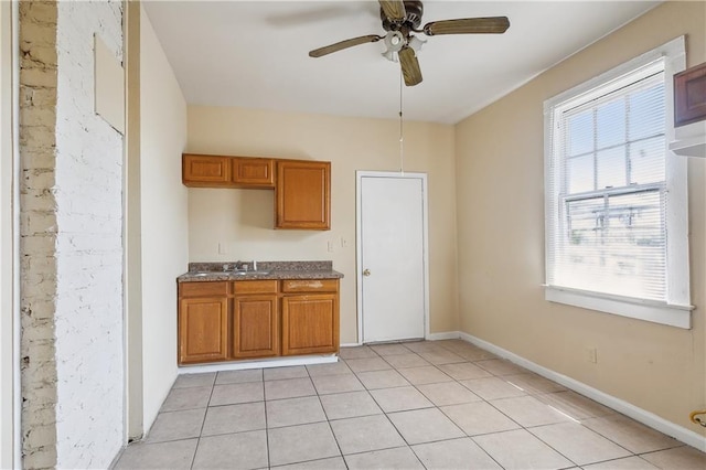 kitchen featuring light tile patterned floors, brown cabinetry, a ceiling fan, a sink, and baseboards