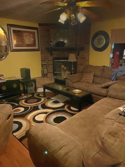 living room featuring ceiling fan, a fireplace, and a textured ceiling