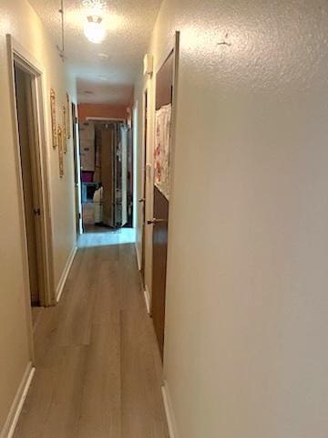 hall featuring light wood-type flooring and a textured ceiling