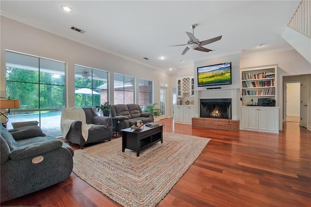 living room with crown molding, ceiling fan, wood-type flooring, and a fireplace