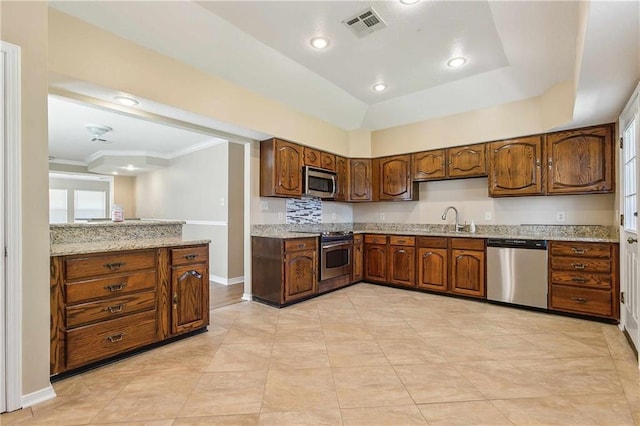 kitchen with sink, ornamental molding, appliances with stainless steel finishes, tasteful backsplash, and light stone counters