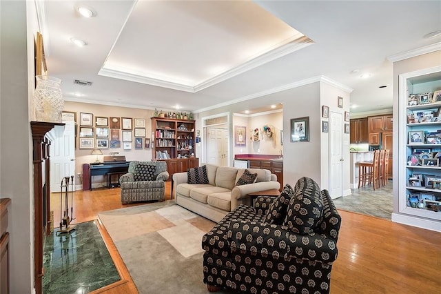 living room featuring crown molding, light wood-type flooring, and a tray ceiling