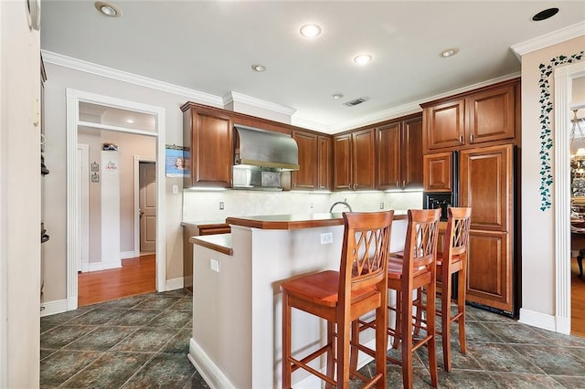 kitchen featuring a kitchen bar, crown molding, wall chimney exhaust hood, and decorative backsplash