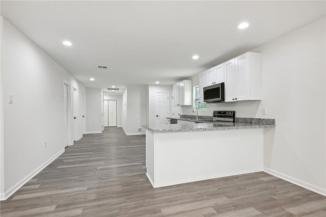 kitchen featuring kitchen peninsula, appliances with stainless steel finishes, stone countertops, white cabinets, and hardwood / wood-style floors