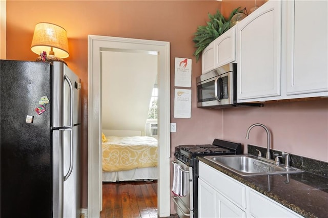 kitchen with sink, wood-type flooring, white cabinetry, stainless steel appliances, and dark stone countertops