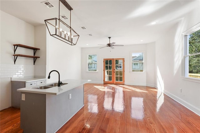 kitchen with light wood-type flooring, backsplash, a center island with sink, and sink