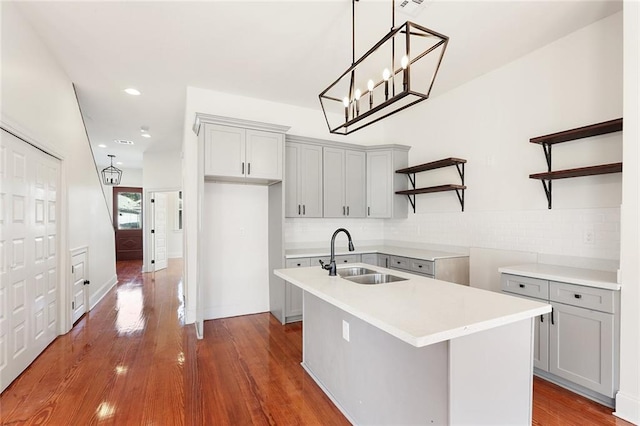 kitchen with hardwood / wood-style floors, sink, decorative backsplash, and a center island with sink