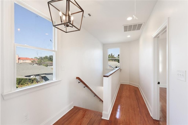 hall with a wealth of natural light, wood-type flooring, and a notable chandelier