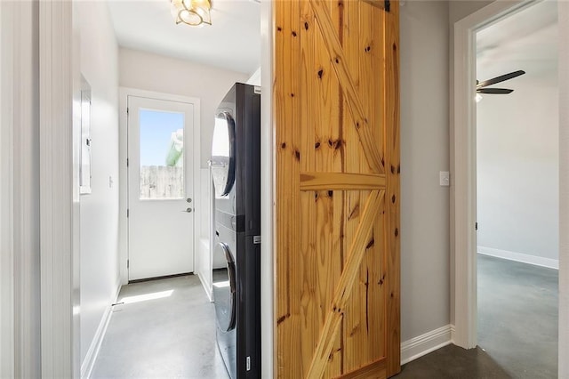 hall featuring stacked washer / drying machine, concrete floors, baseboards, and a barn door