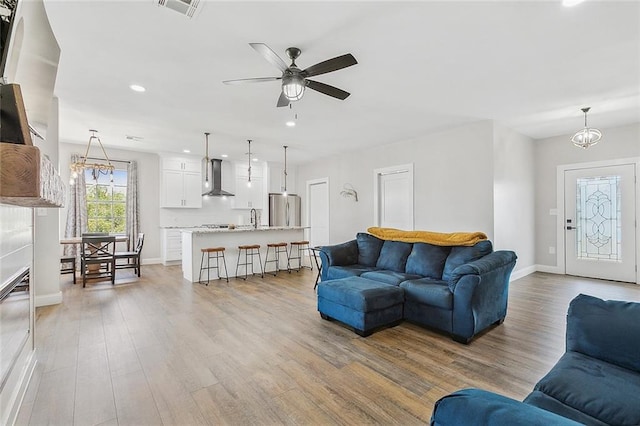 living room with ceiling fan with notable chandelier, sink, and light hardwood / wood-style flooring